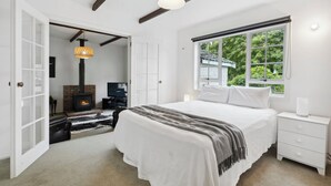 Un dormitorio con una cama grande, chimenea, televisor y ventana con vistas a zonas verdes.