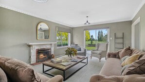 Una sala de estar con chimenea, dos sofás, una mesa de centro y vistas a un jardín a través de grandes ventanales.