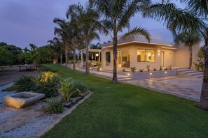 Una casa moderna con un césped cuidado, palmeras y un área de patio.