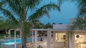 A modern outdoor pool area with lounge chairs, a dining area, and a well-lit interior space.