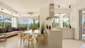A modern kitchen with a central island, large windows, and a dining area with a sofa and chairs.