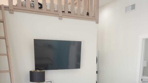 A modern living room with a grey sofa, two blue armchairs, a dark blue cabinet, a TV mounted on the wall, and a ladder against the wall. - New, full Casita in North Phoenix with AC, WiFi (Phoenix)