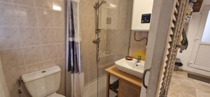 A bathroom with a toilet, shower, sink, and a small shelf with toiletries.