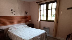 A bedroom with a bed, a nightstand, a window with curtains, a radiator, and a wooden headboard. - Very quiet country house (Les Monts du Roumois)