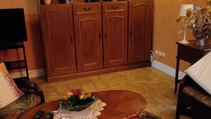A living room with a wooden cabinet, a coffee table with a decorative bowl, a television, and a patterned rug. - Very quiet country house (Les Monts du Roumois)