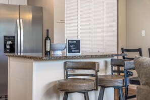 A kitchen with a stainless steel refrigerator, a water dispenser, and a sign that reads "WELCOME ENJOY YOUR GETAWAY". - Monthly Lease Available - Mountain Views, Modern Comfort: Your Cozy Getaway (Colorado Springs)