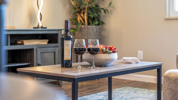 Una mesa de comedor con una botella de vino, dos copas de vino y un bol de fruta.
