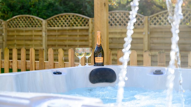 A hot tub with a bottle of Canti Prosecco and two glasses of wine, surrounded by a wooden fence and greenery. - Little Hawkcliffe Retreat | Hot Tub & Parking (West Yorkshire)