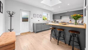 A modern kitchen with grey cabinets, a central island with stools, a skylight, and a view of the outdoors. - Little Hawkcliffe Retreat | Hot Tub & Parking (West Yorkshire)