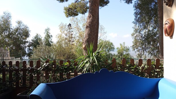A blue bench in a garden area with a fence, trees, and a view of a body of water.