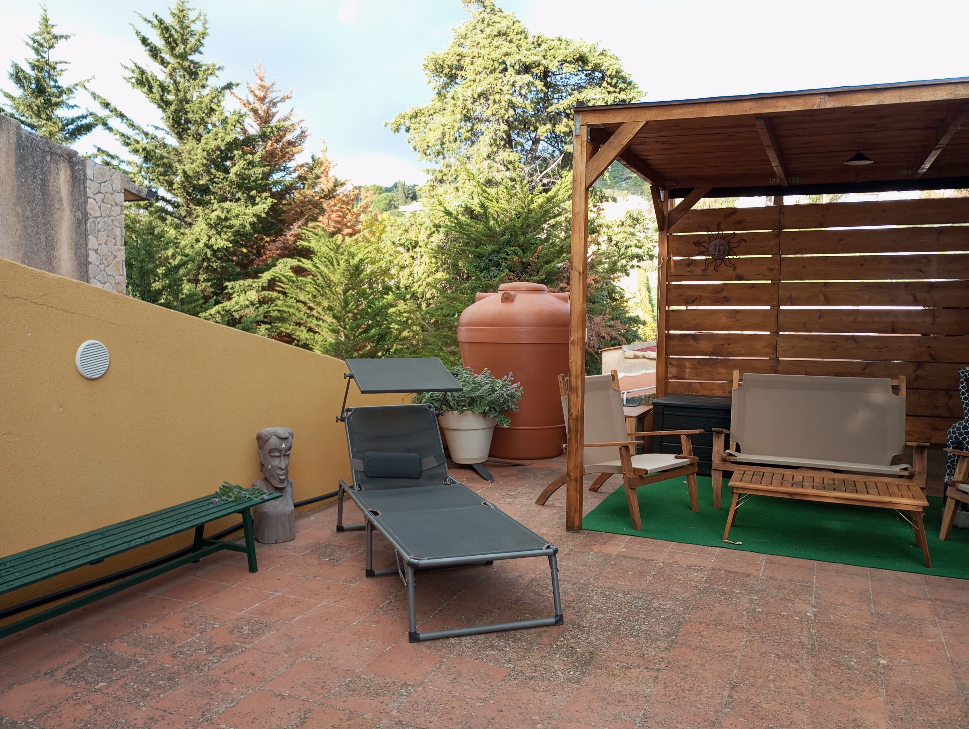Un espace patio comprenant un fauteuil de jardin vert, une table en bois et un coin salon abrité.
