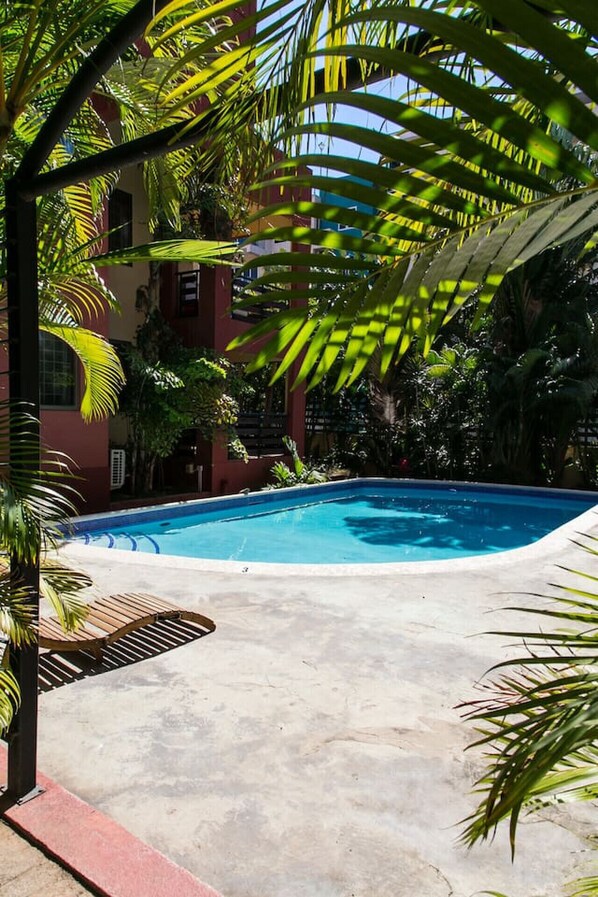 A swimming pool surrounded by palm trees and a building with a red facade.