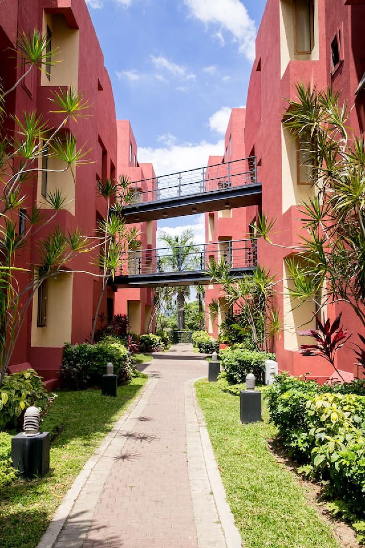 Ein Weg führt zu einem Gebäude mit roter Fassade und einer Fußgängerbrücke.