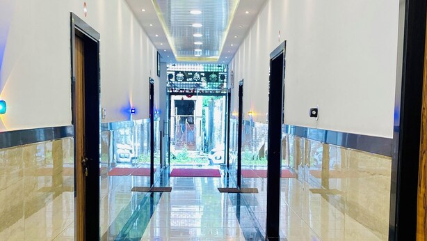 A long, well-lit corridor with a shiny tiled floor, leading to a bright entrance area with a glass door. - Hotel Radhe Shree (Khandwa)