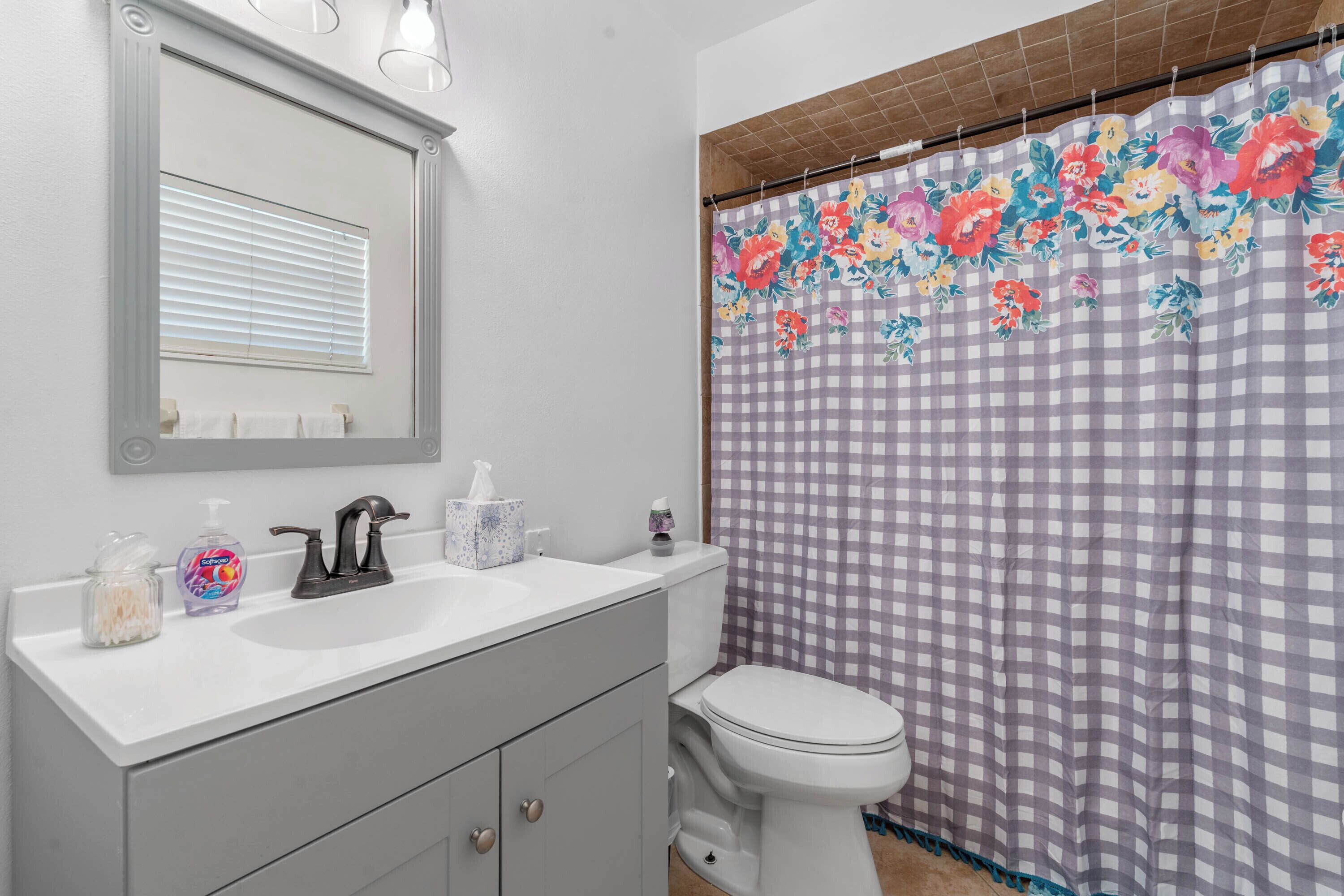 A bathroom with a white sink, a mirror, a toilet, and a floral shower curtain.