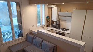 Eine kompakte Küche mit Einbaugasherd, Mikrowelle und Spüle. Es gibt eine kleine Sitzecke mit Sofa und rundem Tisch.