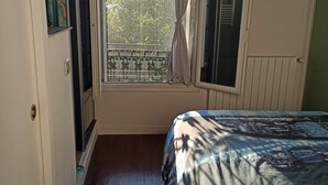 Ein Schlafzimmer mit großem Fenster, einem Bett mit gemustertem Überwurf, Holzboden und einer gewobenen Leuchte.