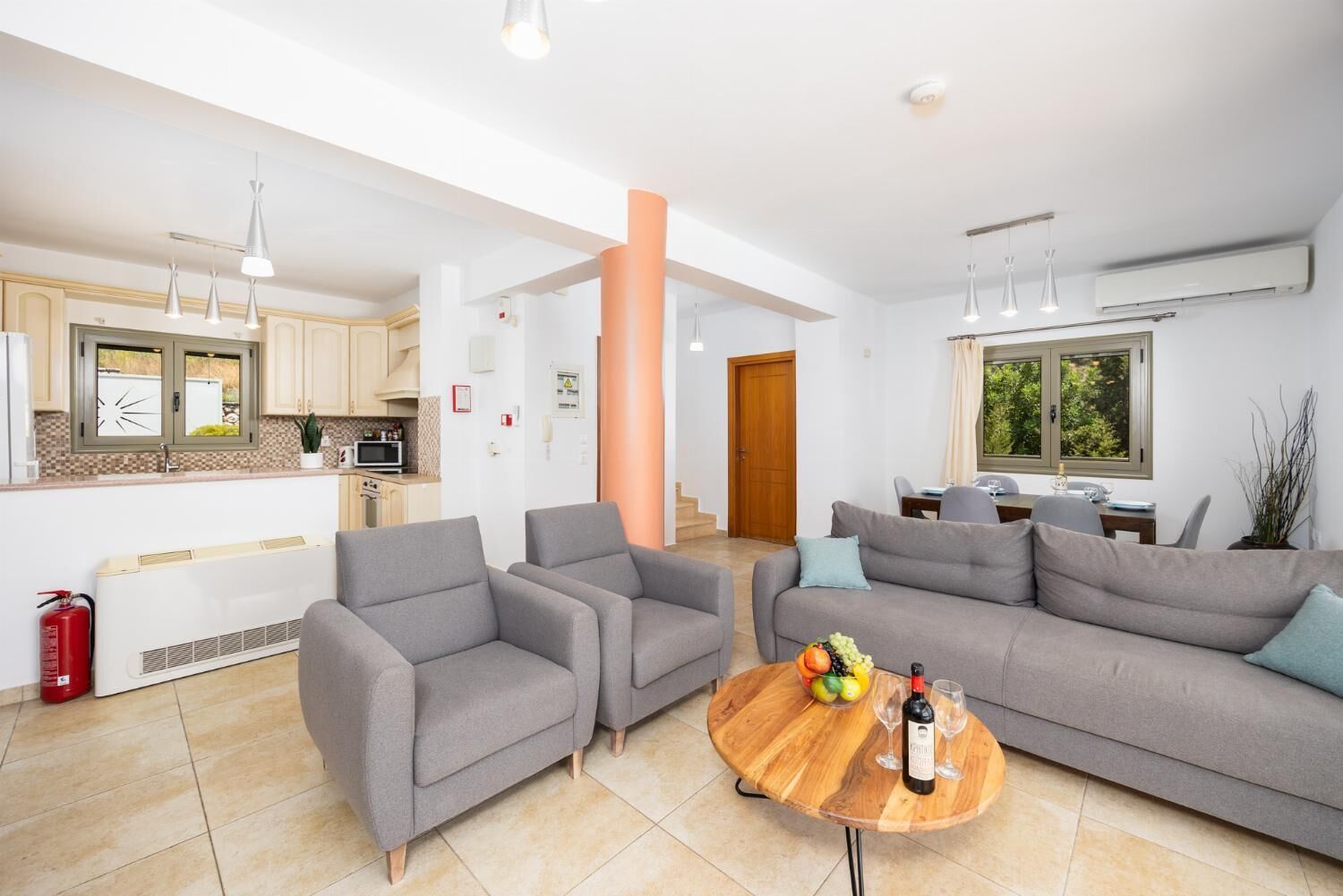 A modern living room with grey sofas, a wooden coffee table, and a kitchen area in the background.