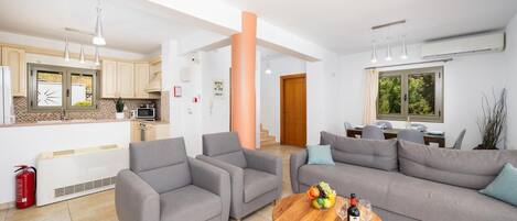 Ein modernes Wohnzimmer mit grauen Sofas, einem Holztisch und einer Küchenzeile im Hintergrund.