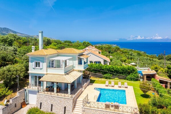 Una casa de dos pisos con piscina, rodeada de vegetación y con vista a un cuerpo de agua.