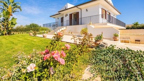 Ein modernes, zweistöckiges Haus mit Balkon, umgeben von einem gepflegten Garten mit verschiedenen Pflanzen und Blumen.