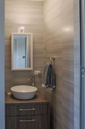 Un baño moderno con un espejo grande, un lavamanos redondo y un perchero para toallas.