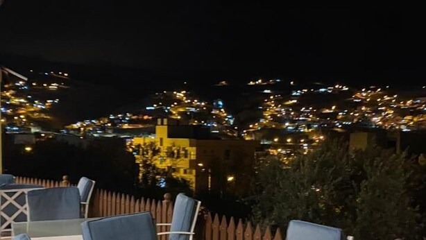 An outdoor seating area with tables and chairs, a wooden fence, and a view of a cityscape at night. - Eighth Wonders Hotel (Wadi Musa)