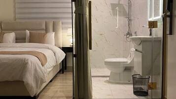Una habitación de hotel moderna con cama, baño con cabina de ducha de vidrio y piso con piso de mármol.
