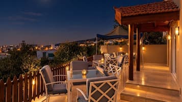 Un patio al aire libre con mesas y sillas, una pérgola de madera y vistas de la ciudad de noche.