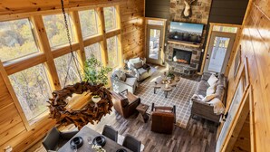A cozy cabin interior with a fireplace, wooden walls, large windows, and a dining area. - Stunning View | Game Room Fun | Hot Tub & Fire Pit (Sevierville)