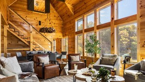 A cozy log cabin interior with a staircase, wooden walls, large windows, and comfortable seating areas. - Stunning View | Game Room Fun | Hot Tub & Fire Pit (Sevierville)
