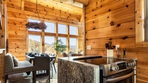 A wooden cabin interior with a kitchen area, dining table, and seating. - Stunning View | Game Room Fun | Hot Tub & Fire Pit (Sevierville)