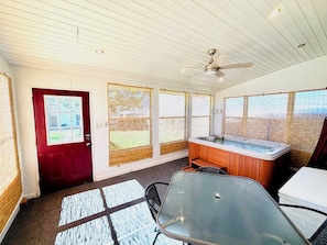 A room with a wooden door, a hot tub, a ceiling fan, and large windows with blinds.