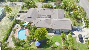 Vue aérienne d’une maison avec piscine, entourée de palmiers et d’une pelouse bien entretenue.