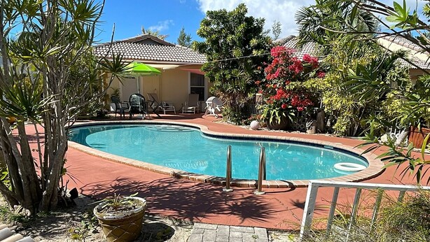 Une piscine dotée d’une terrasse carrelée, entourée de plantes en pot et agrémentée d’un petit espace patio.