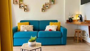 Een woonkamer met een blauwe bank, een bijzettafeltje met een plant en een houten plank met potplanten.
