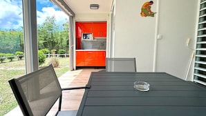 Een balkon met een tafel en stoelen, een rode keuken op de achtergrond en een helder uitzicht op de omgeving.
