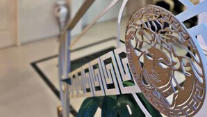 Ein modernes Interieur mit einer Treppe, deren dekorative Metallgeländer ein geometrisches Muster und ein Theatermasken-Emblem aufweisen.