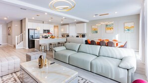 A modern kitchen with white cabinets, a central island, and a dining area with orange chairs.