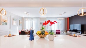 A modern hotel lobby with a central dining area, a seating area with a TV, and a large window with curtains.