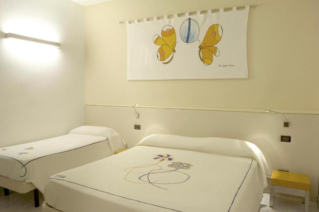 Ein Hotelzimmer mit zwei Einzelbetten, einem kleinen Nachttisch, einem Wandvorhang und einer Lampe.