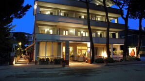A multi-story hotel with a well-lit entrance, outdoor seating, and a visible staircase leading to the entrance. - Hotel Eros Residence (Cervia)