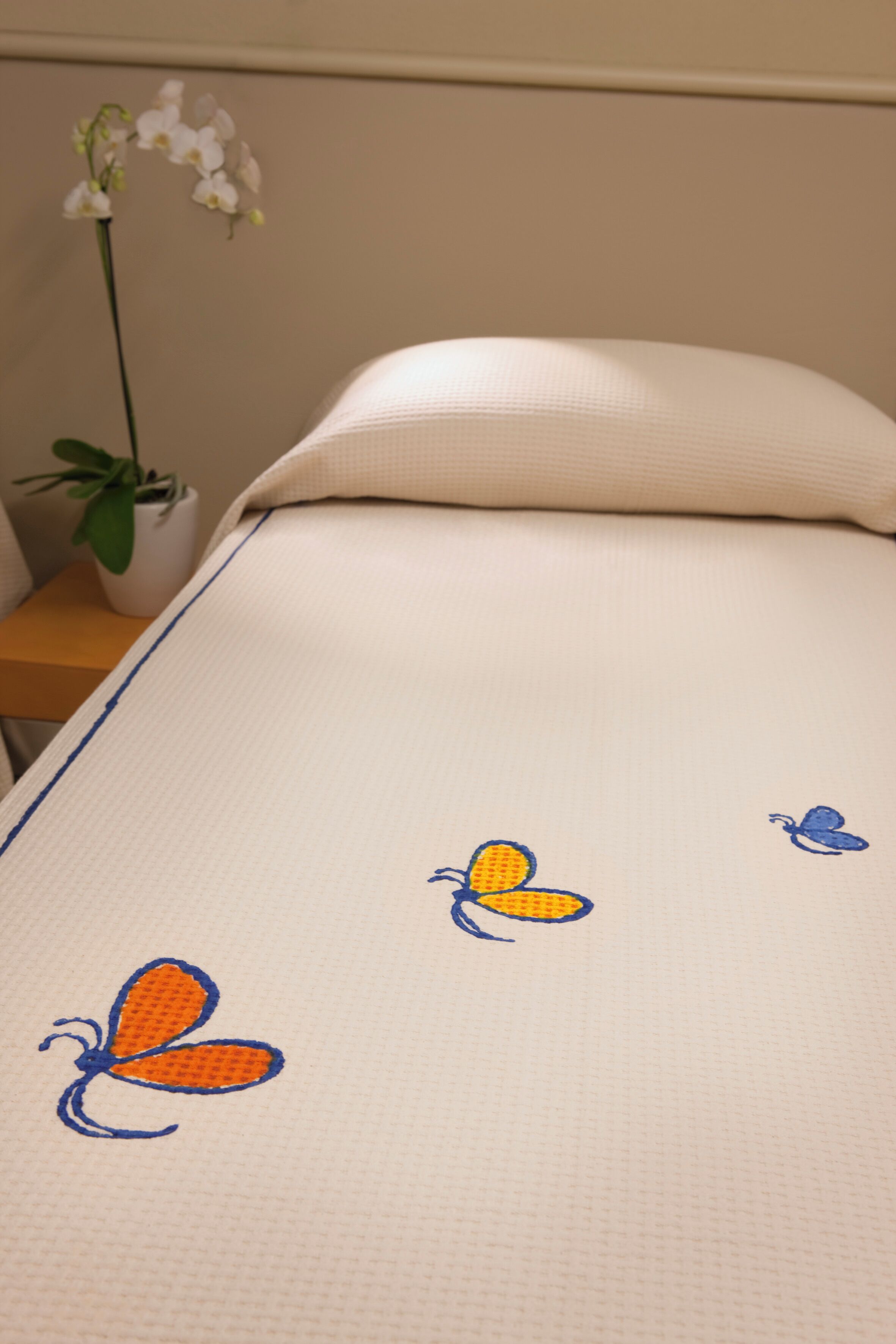 Un lit avec un oreiller blanc et une couvre-lit ornée de motifs de papillons brodés.