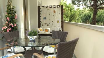 A balcony with wicker furniture, a glass table, and a potted plant.