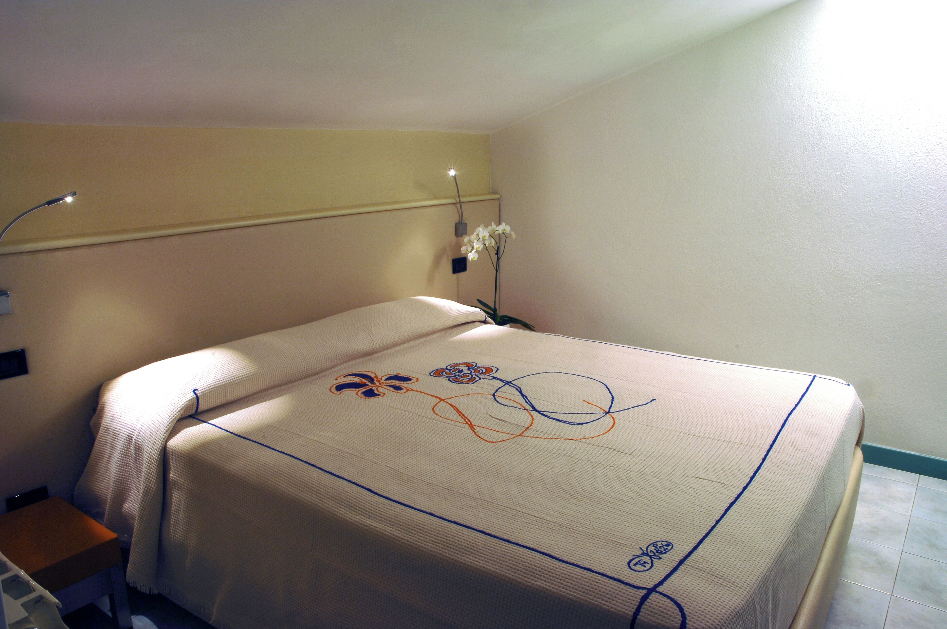 Habitación de hotel con cama, mesita de noche, lámpara y aplique de pared.