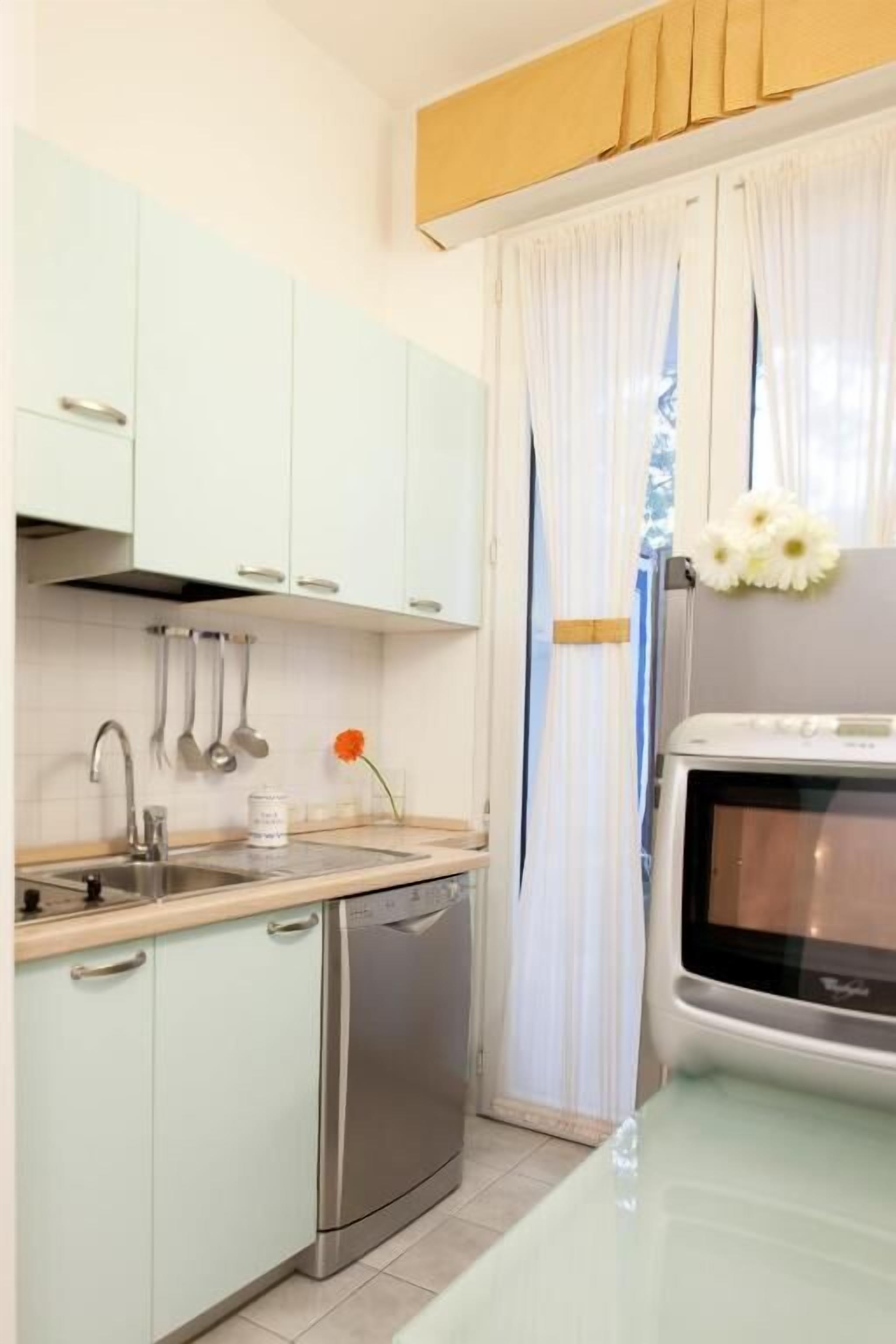 Una cucina compatta con mobili verde chiaro, lavastoviglie in acciaio inox, lavello e un forno a microonde.