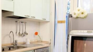 Una cucina compatta con mobili verde chiaro, lavastoviglie in acciaio inox, lavello e un forno a microonde.