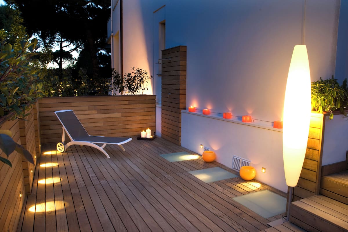 A wooden deck with a lounge chair, candles, and a wall-mounted light fixture.