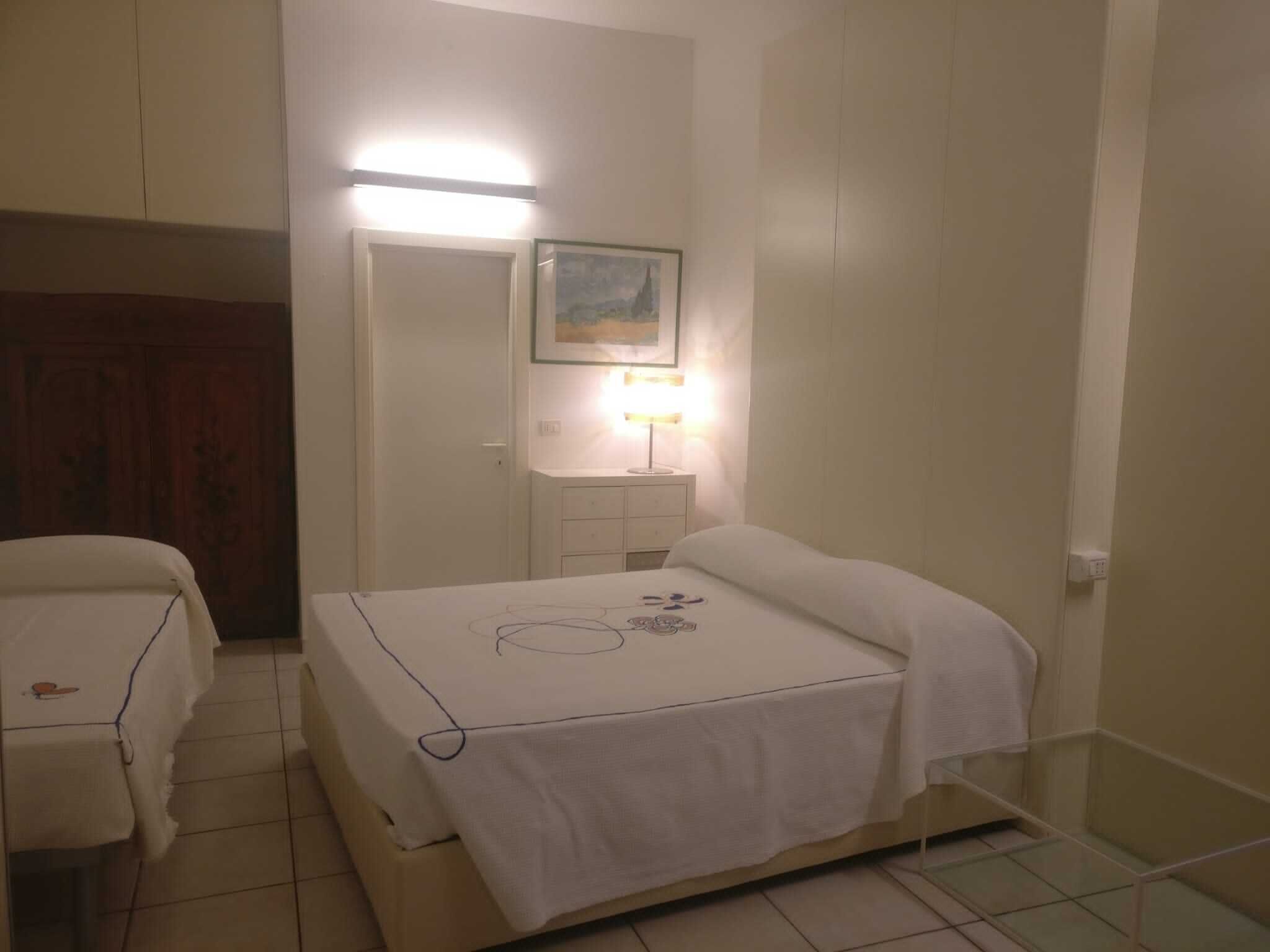 A bedroom with a bed, a bedside table, a lamp, and a mirror.