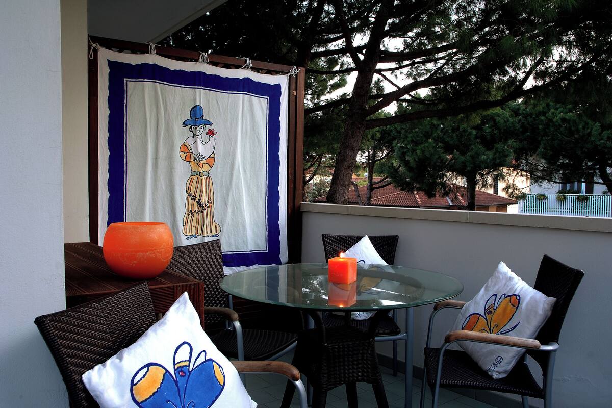 A glass table with a candle, wicker chairs, and a colorful cushion.